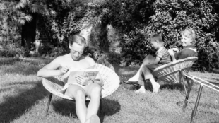 Photo en noir et blanc. On peut voir Michel Foucault au premier plan, assis, dans le jardin, en train de lire, et derrière sa mère également assise avec sur ses genoux le neveu de Michel Foucault
