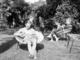 Photo en noir et blanc. On peut voir Michel Foucault au premier plan, assis, dans le jardin, en train de lire, et derrière sa mère également assise avec sur ses genoux le neveu de Michel Foucault