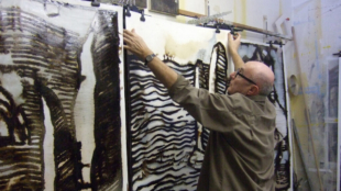 L'artiste Bernard Decourchelle dans son atelier où on le voit suspendant une toile.