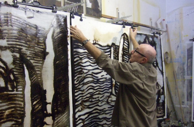 L'artiste Bernard Decourchelle dans son atelier où on le voit suspendant une toile.